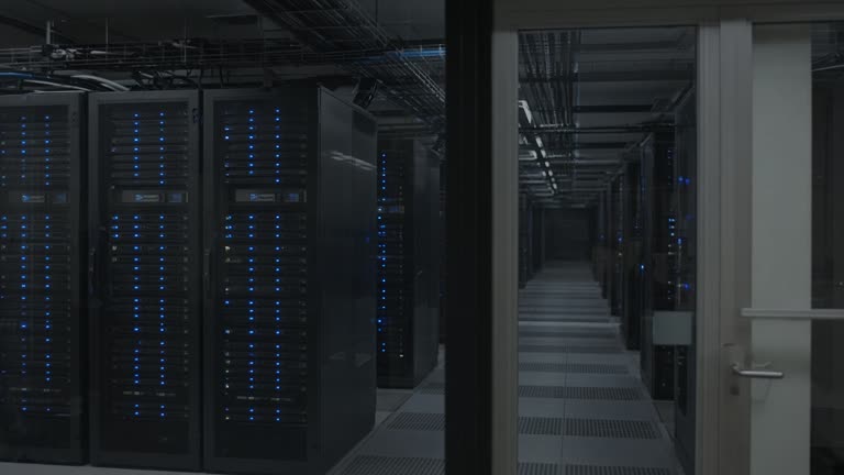 Server room aisle with blue status lights and cable trays, shot through glass without readable labels, no logos