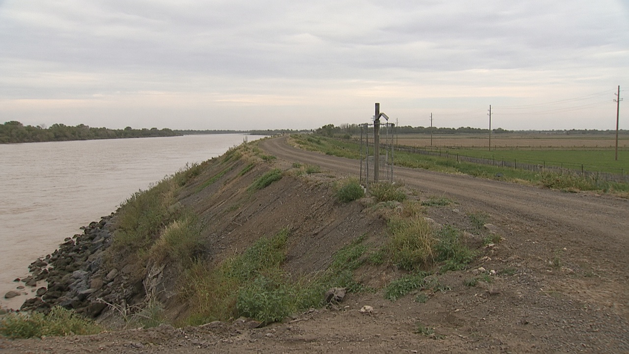 Murray River town levee with farmland and a fenced pipeline marker post in middle distance under hazy afternoon light, no logos or readable text