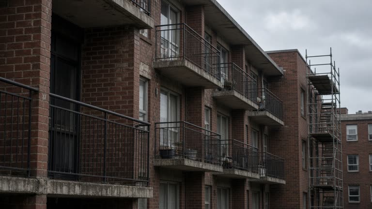 Public housing apartment balcony in Melbourne with brick facade and overcast sky, maintenance scaffold in background, no readable signs or logos