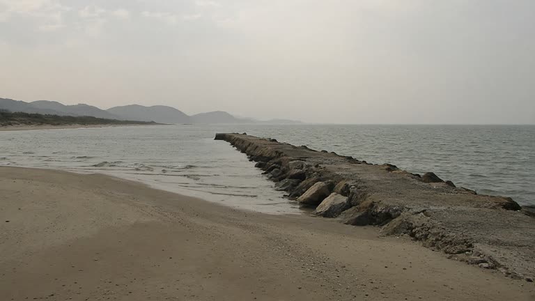 East Sea coastline near Wonsan under hazy afternoon light, empty beach and breakwater, distant grey horizon, no missiles or logos, no readable text