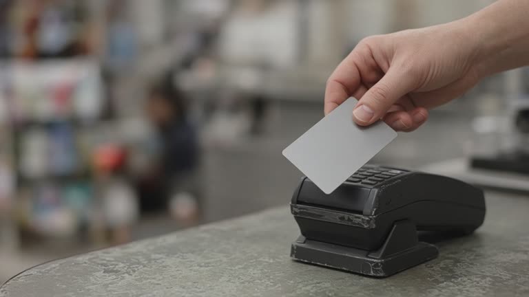 Payment terminal on a retail counter with a hand holding a generic metal credit card, shallow depth of field, muted store lighting, no logos or readable text