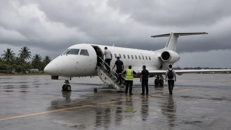 Small regional jet on a tropical airport apron with ground staff guiding passengers up mobile stairs, heavy grey cloud on the horizon, damp tarmac reflections, no logos or readable text.