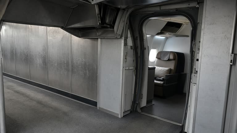 Airport jet bridge interior with a business-class seat visible through the cabin door, grey carpet and brushed aluminium panels, monsoon grey light through terminal glass, luggage bins slightly open, no logos or readable text
