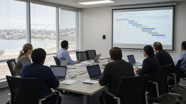 Wollongong council IT meeting room with projected blurred Gantt chart, laptops on table, coastal light through blinds, no readable text or logos