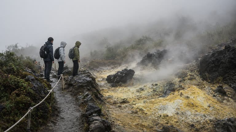 Hikers pausing near yellow-stained sulfur vents on a misty Yangmingshan trail with rope guides along the path, damp volcanic rock and low cloud cover, no logos or readable text