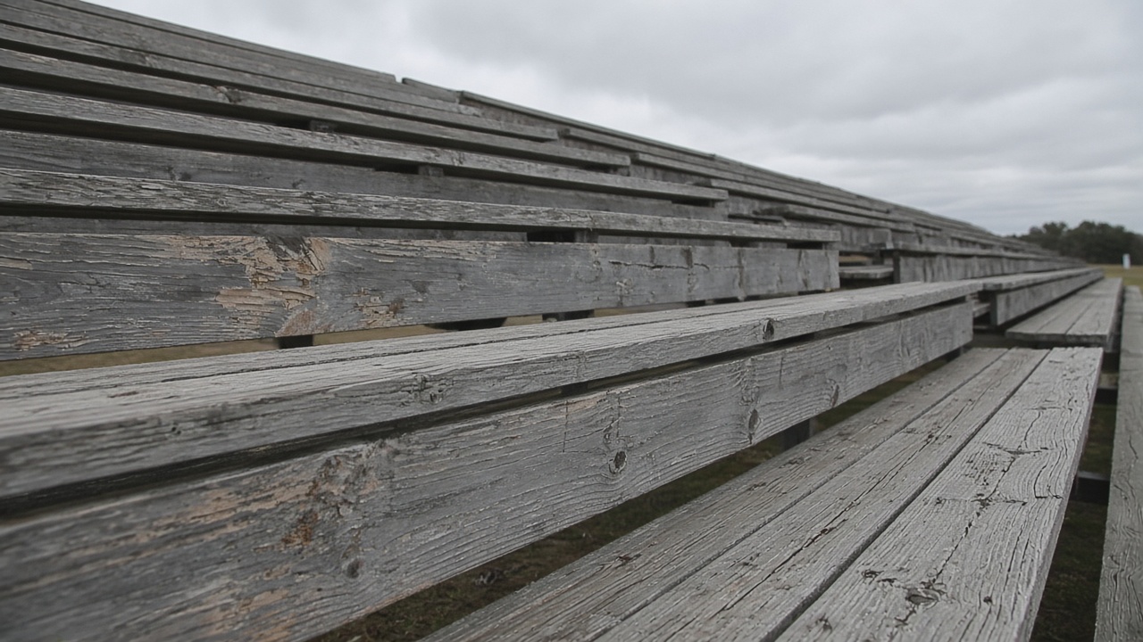 Empty scuffed wooden bleacher plank in overcast daylight, no people, no logos, no readable text