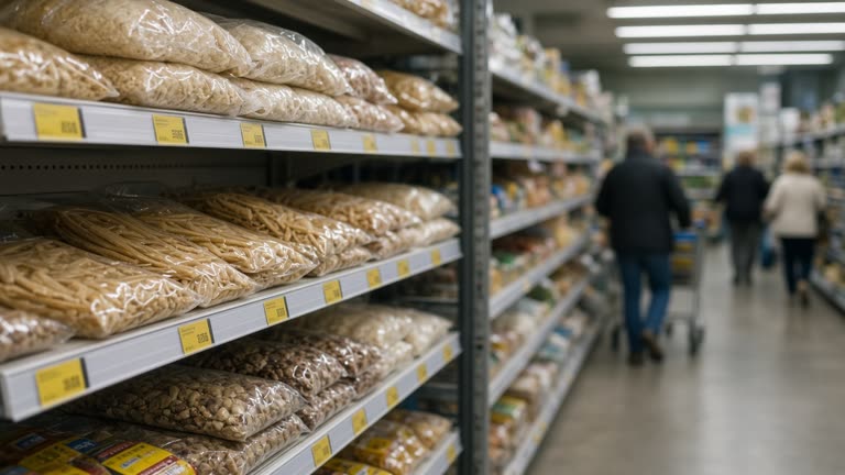 Australian supermarket grocery aisle with yellow promotional shelf tags on packaged goods, fluorescent overhead lighting, shoppers blurred in background, documentary wire photo, no logos or readable text