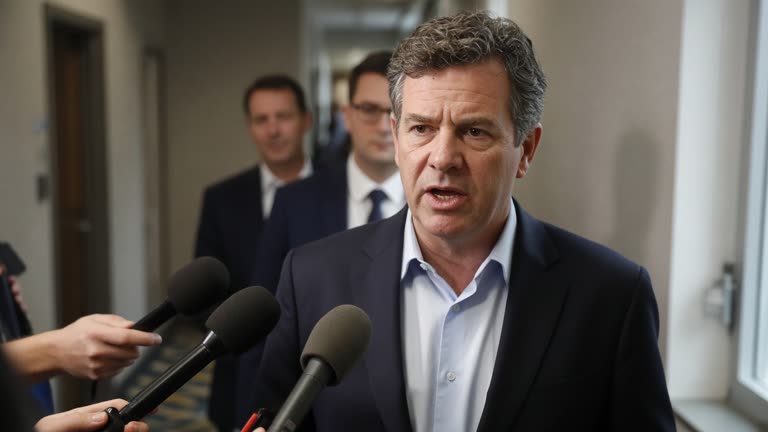 Australian prime minister speaking to reporters in a hotel corridor with neutral walls, handheld microphones extended toward him, aides blurred behind, fluorescent and window light mix, no readable logos on microphones