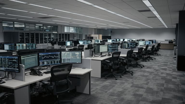 Investment bank trading floor with rows of monitors and empty chairs before the open, cool fluorescent light on carpet tiles, no logos or legible screen text.