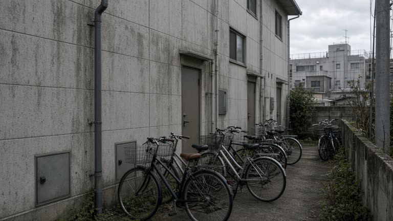 Modest apartment building exterior in a Japanese industrial town, bicycles parked outside, overcast afternoon light, no readable signage or logos