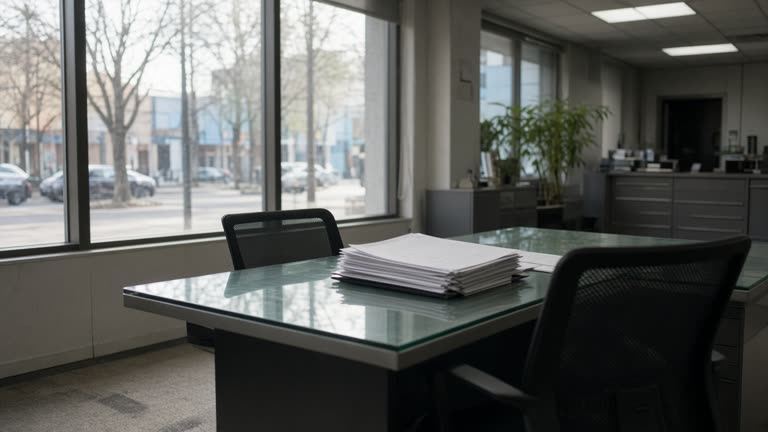 Bank branch interior with glass consultation desk and printed home-loan rate sheets turned face-down, afternoon light through street windows, documentary wire photo, no logos or readable text