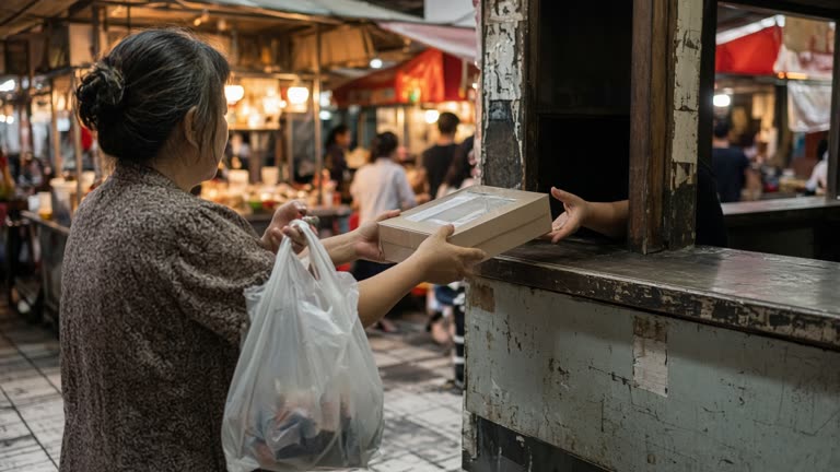 Shopper holding a sealed skincare gift box at a Tainan night market pickup counter with warm lantern light on food stalls in the background, plastic shopping bags and worn tile floor, no logos or readable text