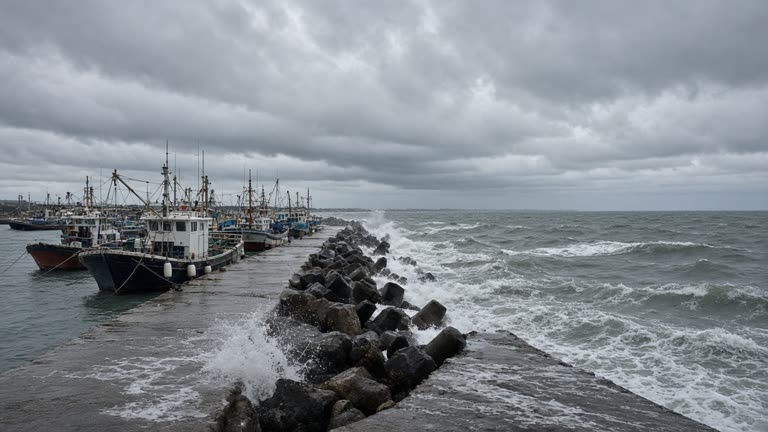 Fishing boats lashed to a concrete pier as grey swells crash against Okinawa seawall under low storm clouds