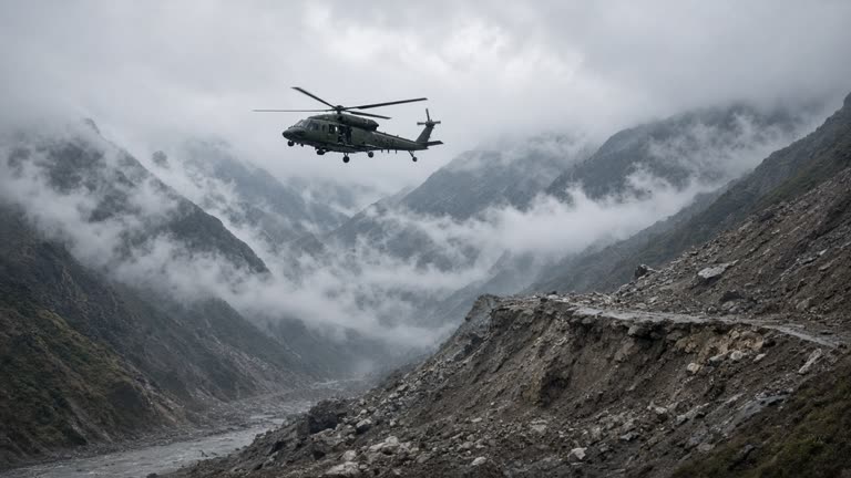 Indian Army helicopter hovers over a misty Himalayan valley near landslide debris, telephoto disaster wire photo