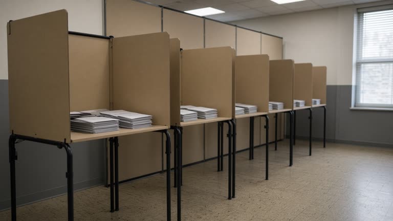 Community center room with folding partition voting booths, stacked paper ballots in neutral envelopes, morning light through blinds, linoleum floor, no logos or readable text.