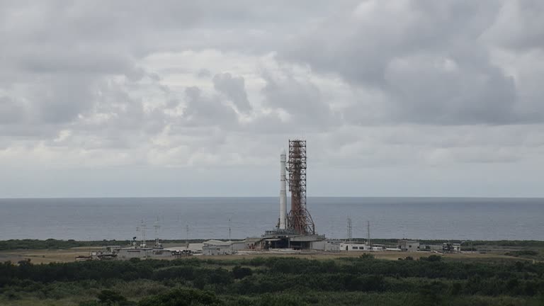 Rocket on a launch pad at Tanegashima Space Center viewed from a distance, ocean horizon and cloudy sky, no logos or readable text