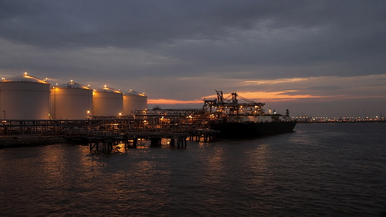 Row of white LNG storage tanks and jetty at Gulf Coast export terminal at dusk, sodium lighting, tanker silhouette, no readable signage