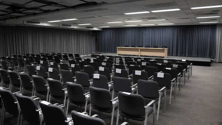 New Delhi convention centre auditorium with rows of empty chairs and stage curtains, fluorescent lighting and scattered delegate lanyards on seats, no logos or readable text