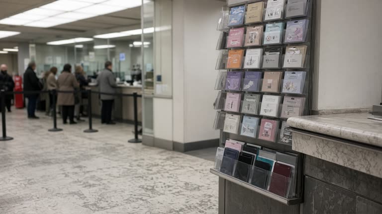 Bank branch interior with a gift card rack beside a service counter under flat fluorescent light, marble floor scuffs, customers blurred in queue, no logos or readable text