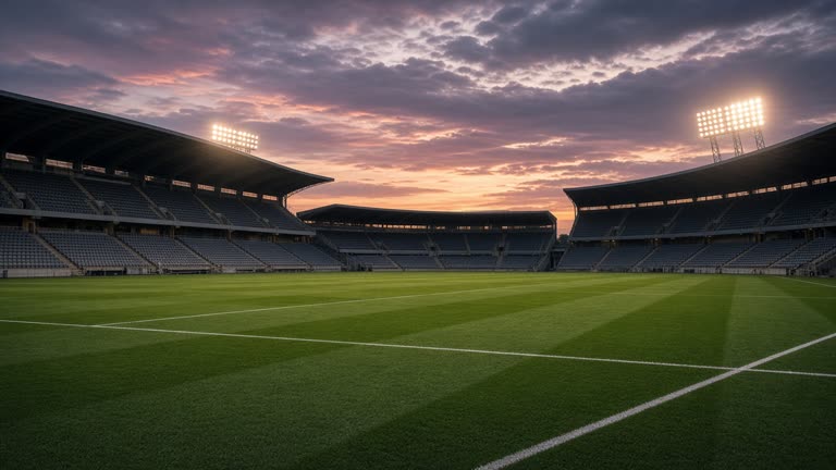 Empty rugby league stadium at dusk with floodlights warming up, green pitch, no logos or readable text