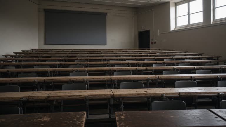 Empty university lecture hall tiered seating, afternoon light through high windows, scuffed wooden desks, no logos or readable slides on screen.