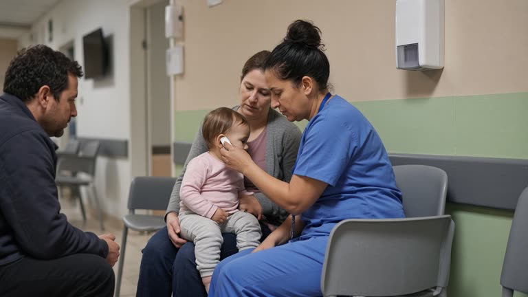 Pediatric nurse checking a toddler's temperature at a hospital ward desk with parents seated on plastic chairs and a wall-mounted hand sanitizer dispenser, soft corridor lighting and pastel paint, no logos or readable text