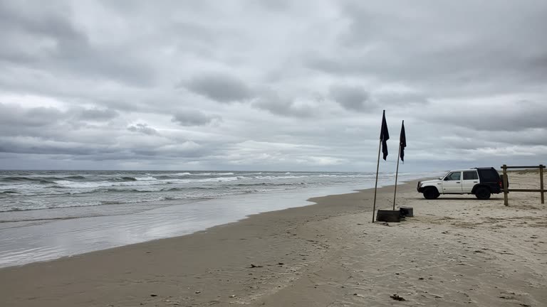 Empty surf beach with closed flags and surf rescue vehicle parked on sand, grey Indian Ocean swell, overcast Perth morning light, no logos or readable text