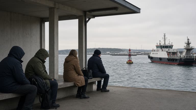 Passengers waiting under cover at a ferry terminal, grey sea and moored vessel beyond, wave-height sensor buoy visible in channel, flat autumn light, no logos or readable text