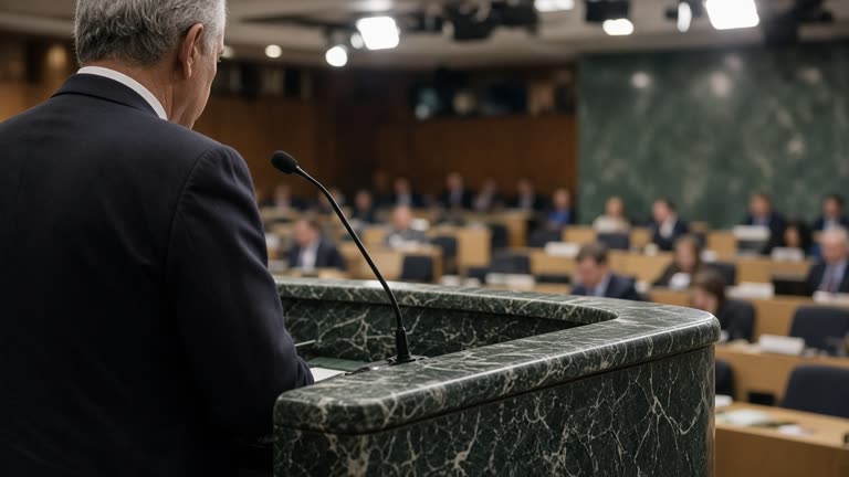 UN General Assembly podium with single microphone and green marble backdrop, delegate floor with rows of desks slightly out of focus, broadcast lights overhead, no flags or readable country nameplates