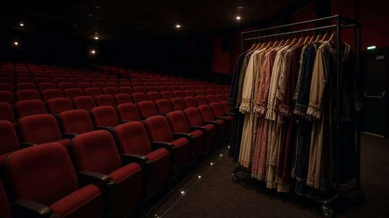 Empty cinema auditorium with red seats and a period costume rack in the aisle under dim safety lighting, no logos or readable text