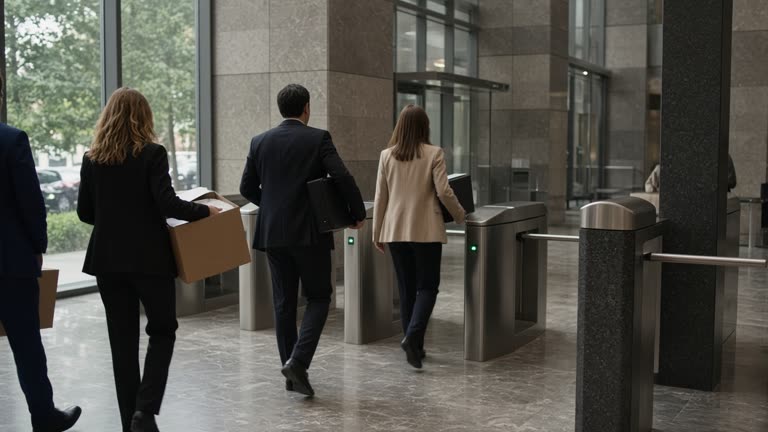 Office tower lobby with a small group of workers in business attire carrying document boxes toward turnstiles, muted daylight, marble floor, no readable logos