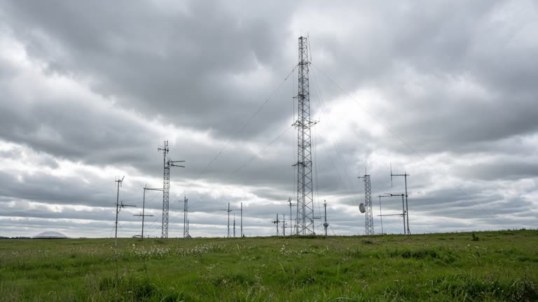 Scientific antenna arrays on a grassy Oxfordshire field under cloudy skies, metal masts and cables, documentary wide shot, no people, no readable text
