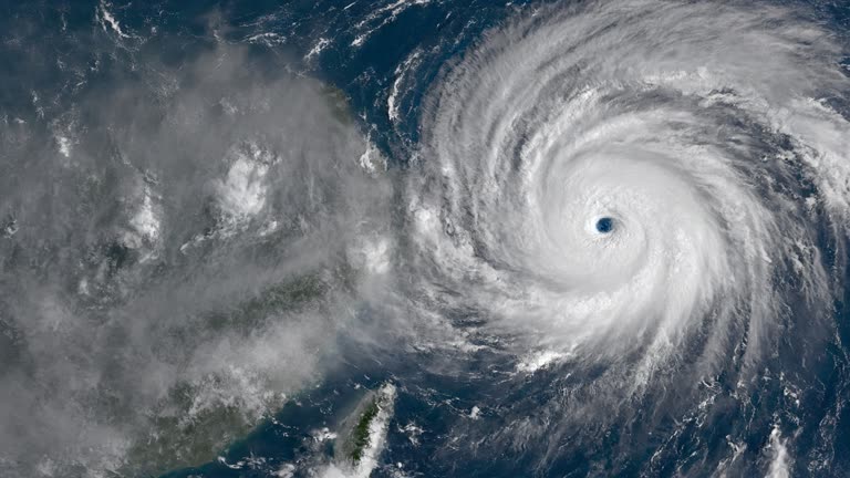 Photoreal high-altitude view of a dense spiral typhoon cloud mass over the western Pacific with a separate broad band of grey monsoon rain cloud sliding toward Taiwan's northern coast, cool blue ocean beneath, no logos or readable text