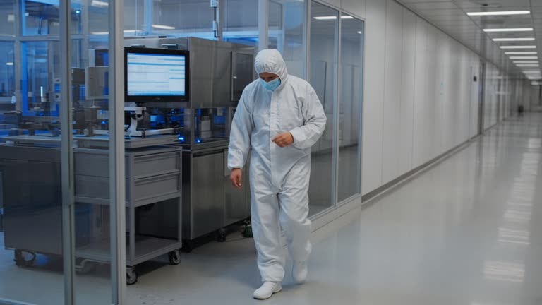 Engineer in clean-room coveralls walking a semiconductor fab corridor beside lot-tracking monitors with soft blue ambient light and polished floors, display text illegible, no logos or readable text