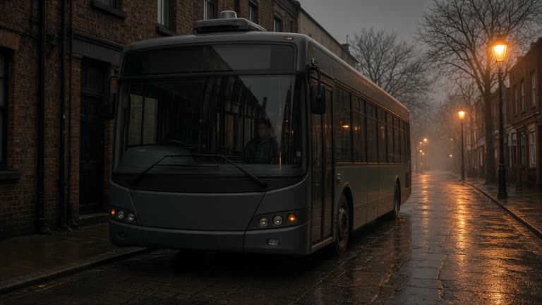 Single-deck bus with roof sensor pod on a misty Camden side street, sodium street lamps, wet pavement reflections, safety driver visible through windscreen, no logos or readable text