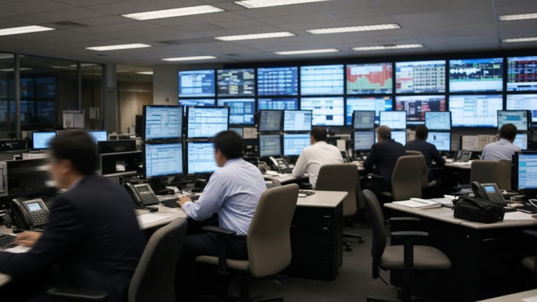 Wide view of an Australian stock exchange dealing room with traders at desks facing rows of market monitors, fluorescent lighting, slight motion blur, no readable text on screens