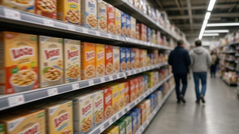 Supermarket aisle with cereal boxes and price shelf tags under cool fluorescent lighting, shoppers blurred in background, no readable brand logos or text
