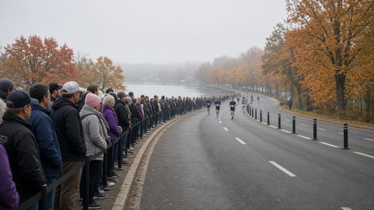 Crowds lining a closed urban lakefront road with runners in the distance and orange fall trees, cool morning haze, handheld documentary framing, no readable banners or bib numbers