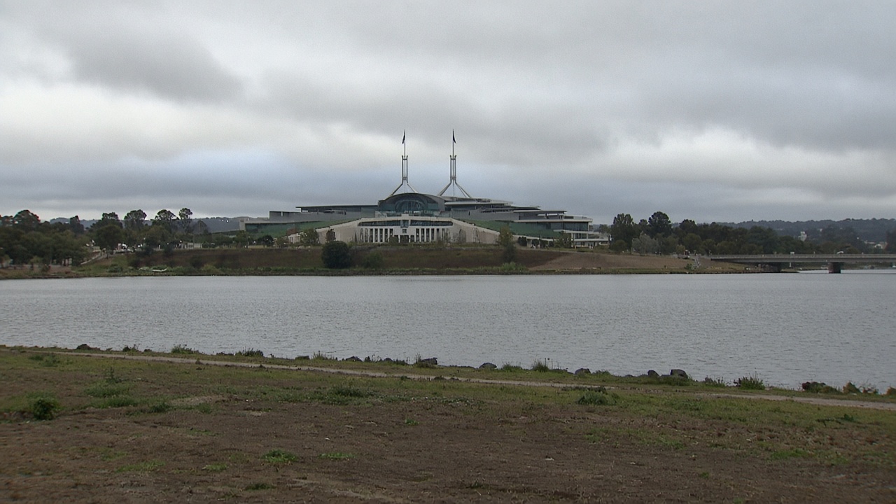 Canberra Parliament House across Lake Burley Griffin on an overcast morning, flagpoles without readable flags, no people in foreground