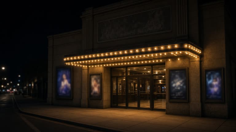 Single-screen cinema facade at night with incandescent marquee bulbs and poster frames showing blurred artwork, empty sidewalk, no readable titles