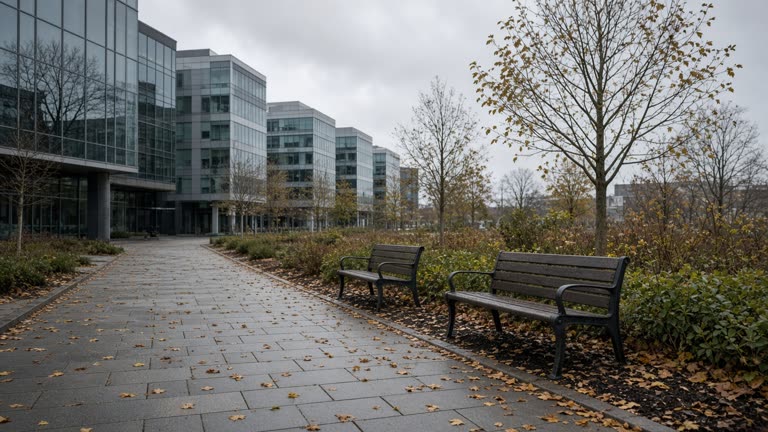 Modern Pangyo office park walkway with glass buildings and empty benches under grey sky, fallen leaves on pavement, no people faces, no logos or readable text