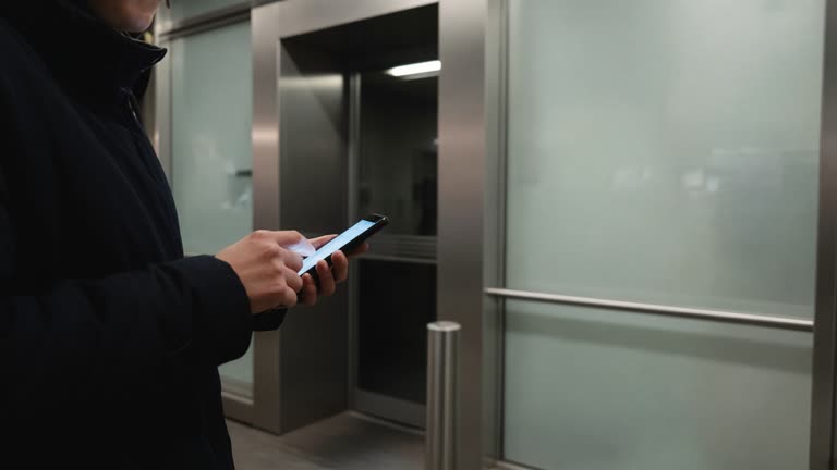 Customer holding a smartphone near a bank ATM vestibule with frosted glass and matte metal surfaces, screen glow on hands only, no logos or readable text