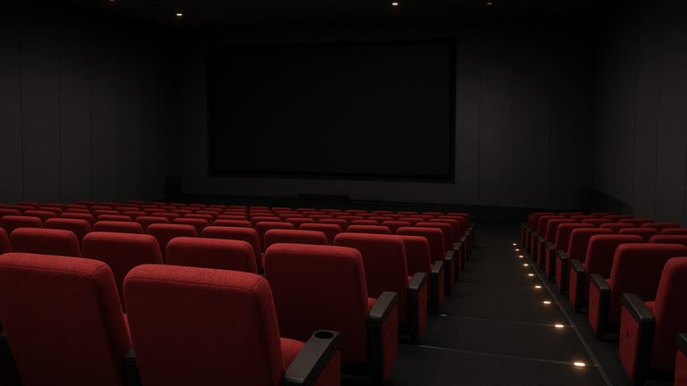 Empty movie theater auditorium with red fabric seats sloping toward a dark screen, dim aisle lighting, no posters or readable text