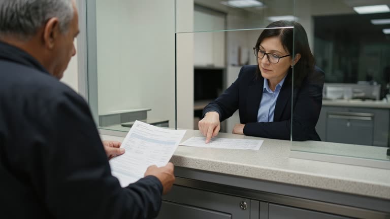 Customer at a bank counter reviewing a paper statement with a adviser pointing at a calendar, fluorescent branch lighting, no logos or readable text.