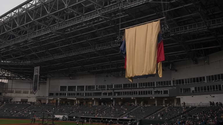 Indoor baseball stadium ceiling with a large championship banner being raised, crowd lights dimmed, flags without readable text, no logos or readable text