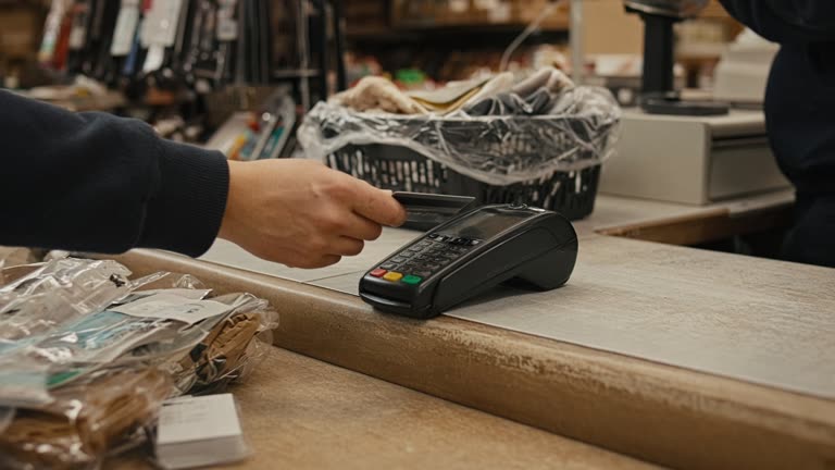Retail store checkout with a card payment terminal on a cluttered counter, shopper hand holding a payment card near the reader, warm indoor lighting, no readable branding