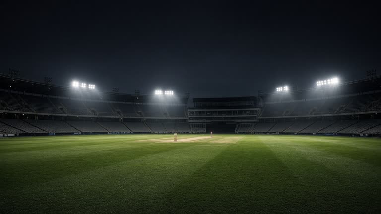 A floodlit cricket stadium outfield at night with empty stands and wicket lights, dewy grass, dark sky, no players facing camera, no logos or readable text