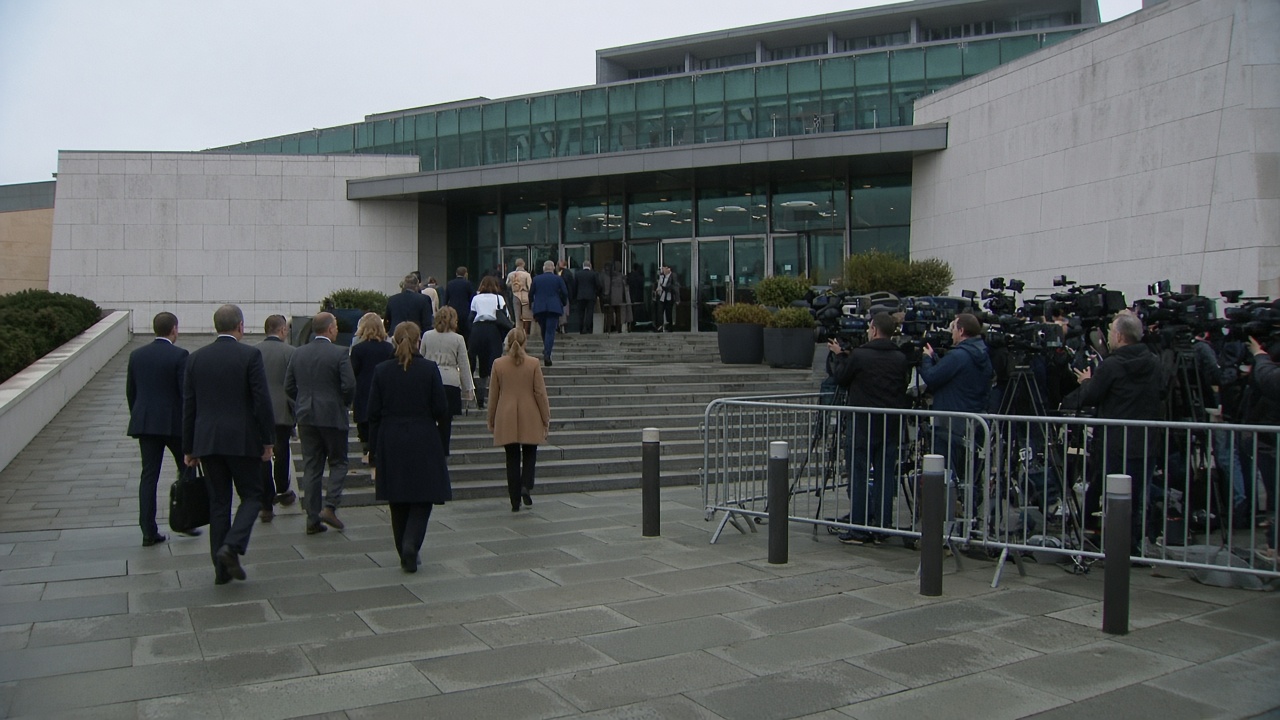 Members of parliament file into Canberra’s Parliament House on an overcast morning as media crews film from the lawn amid security barriers.