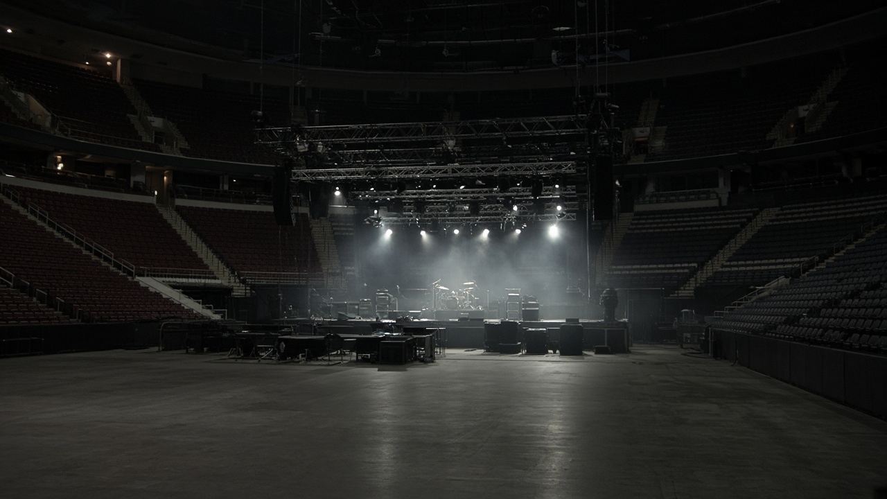 Indoor concert arena empty seats facing a lit stage with truss lights and fog haze, no logos or readable text