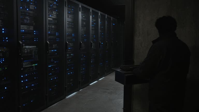 Government data-center aisle with server racks and blue status LEDs, technician silhouette from behind at keyboard, no readable text or faces